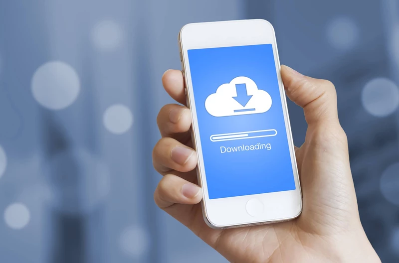 One hand is holding a cell phone that is currently downloading something